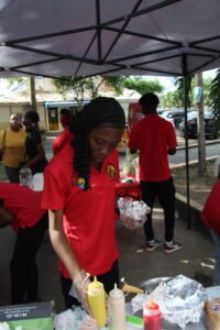 Productions and Operations Management Seminar fundraiser from the School of Business at the Utech Papine Campus on November 27th, 2025 Woman in red taking an order for a hotdog